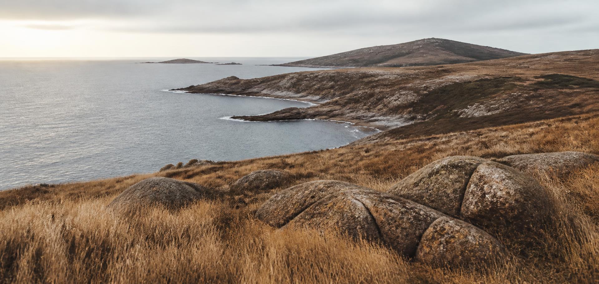 Rugged Australian coastal headland with dry golden grass and granite boulders